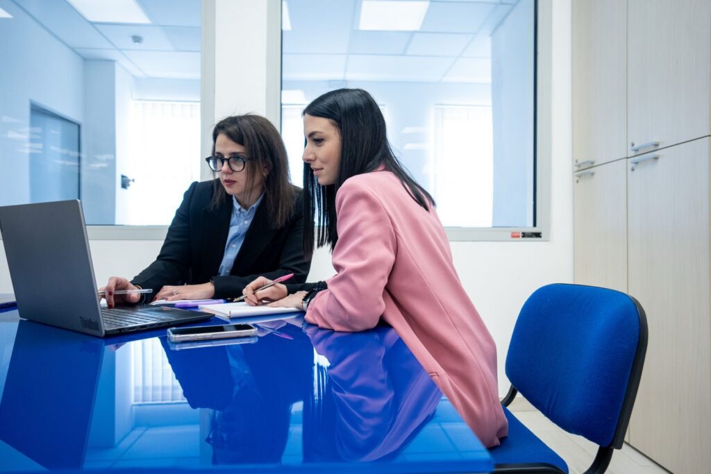 Fotografia di due ragazze di Sinapsys intente a lavorare insieme alla scrivania dell'ufficio