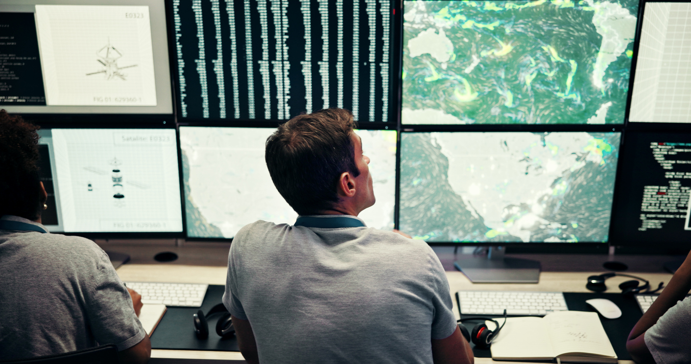 Operatori in una sala di monitoraggio osservano dati ambientali e mappe meteorologiche su più schermi per l’analisi e la previsione dei fenomeni climatici.