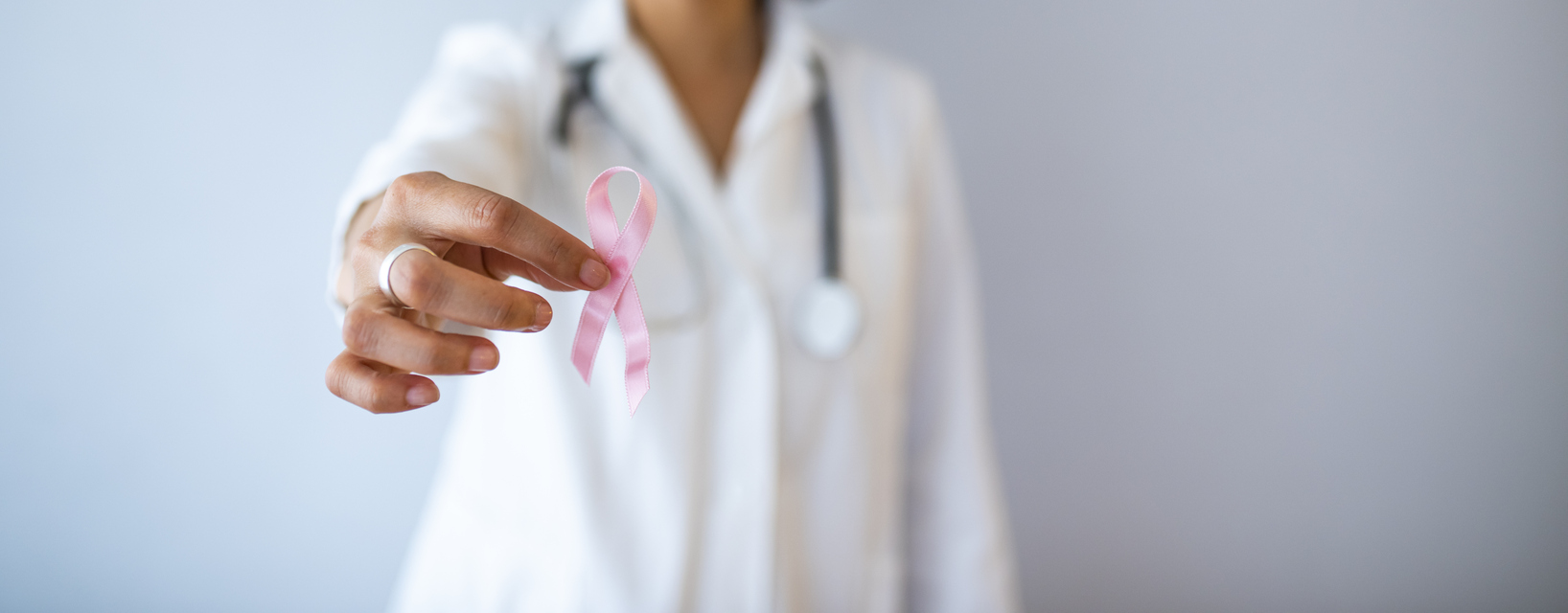 Una persona in camice bianco con stetoscopio mostra un nastro rosa, simbolo della sensibilizzazione sul tumore al seno.
